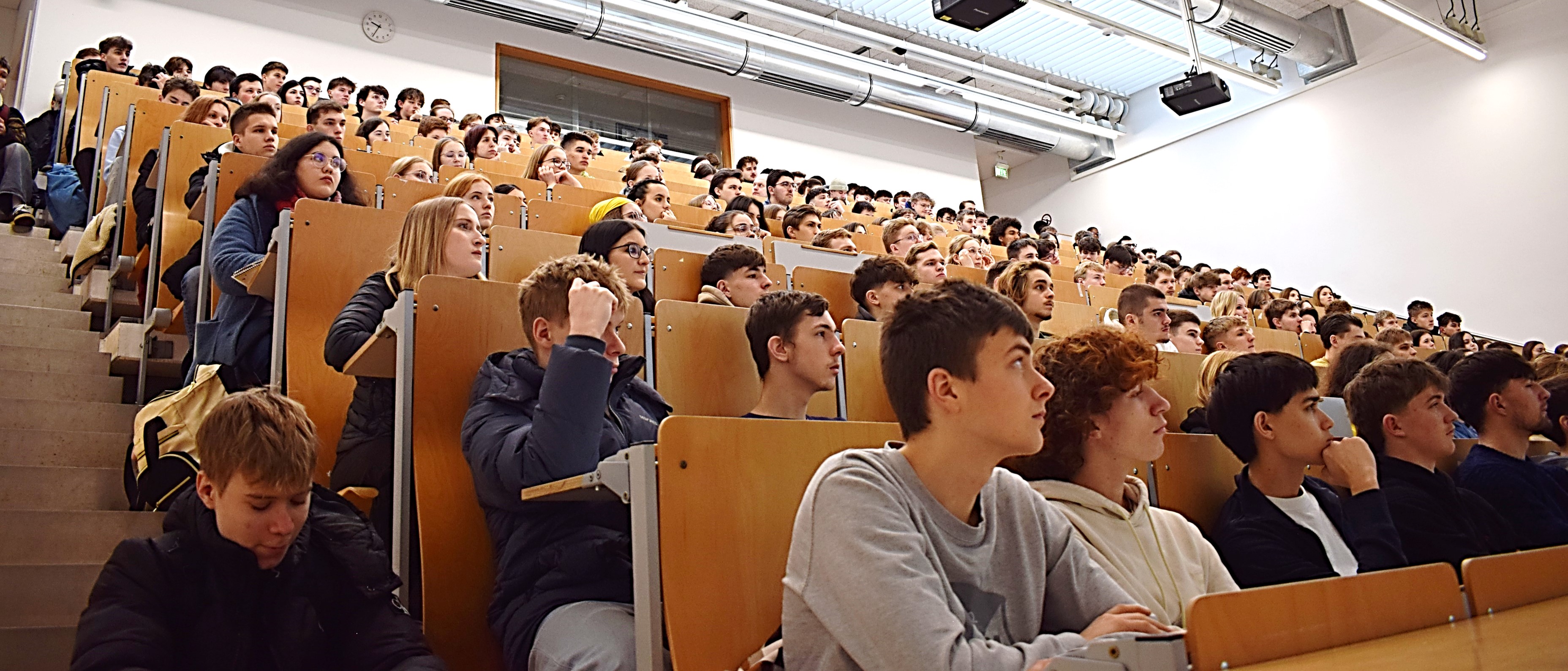 Numerous pupils listen in the lecture hall.